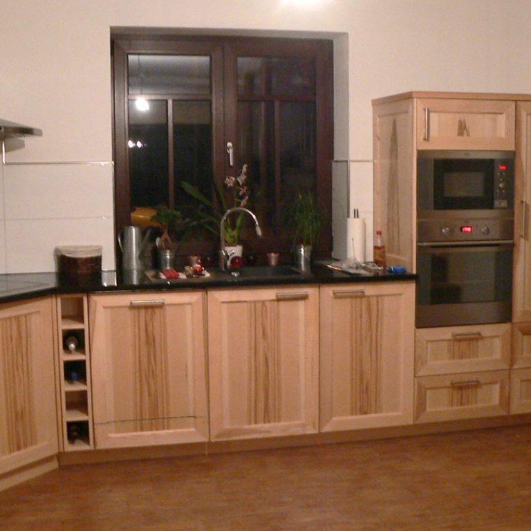 Küche nach Maß mit Holzfronten und moderner Ausstattung Maßgefertigte Küche mit hellen Holzfronten, schwarzen Arbeitsplatten, integriertem Backofen, und großzügigem Stauraum.