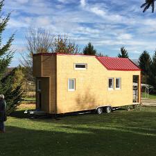 Tiny House aus Holz mit rotem Dach auf Wiese