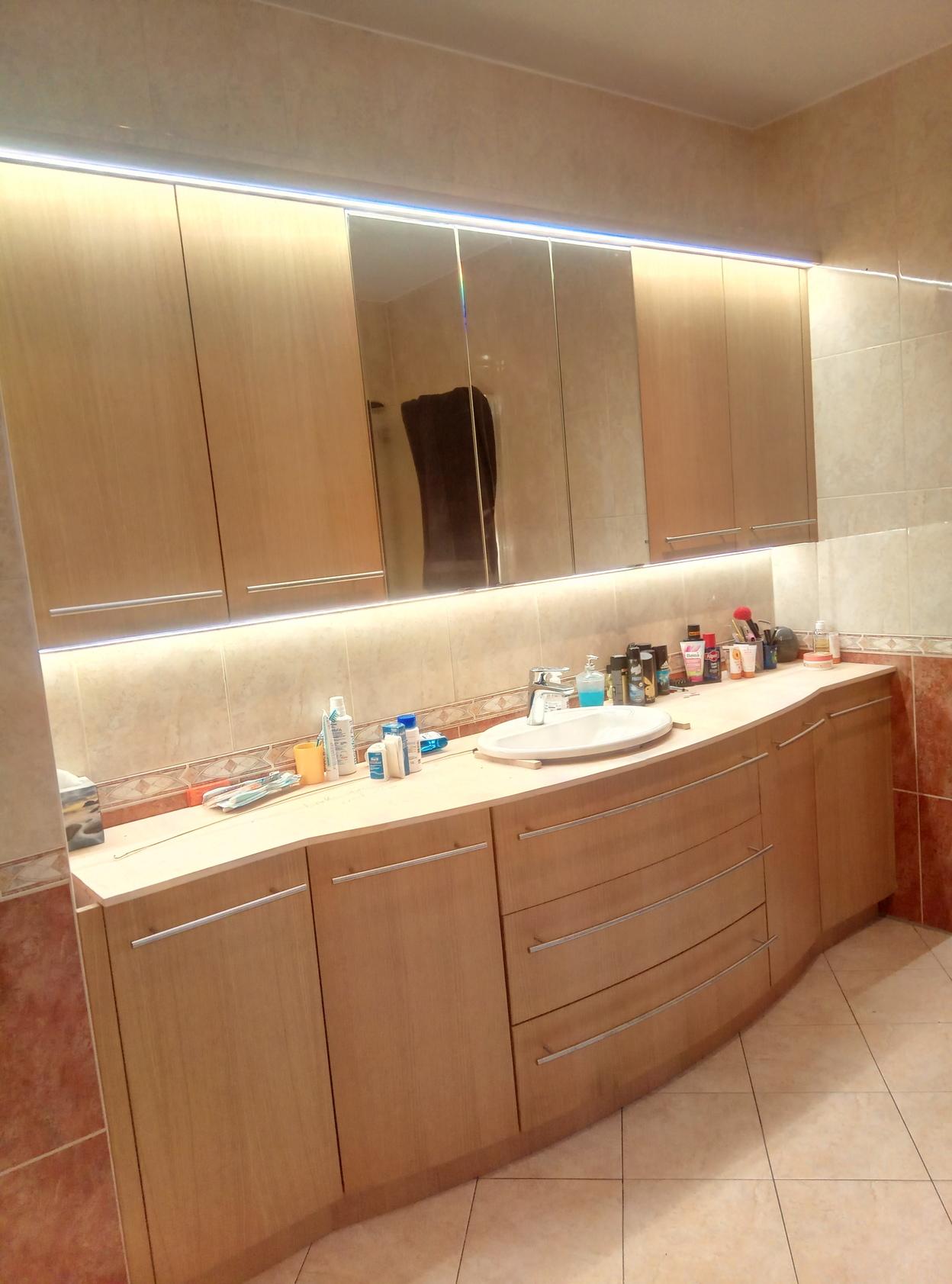 Eleganter Badezimmerschrank nach Maß mit geschwungenen Holzfronten, großem Spiegel, LED-Beleuchtung und großzügigem Stauraum.